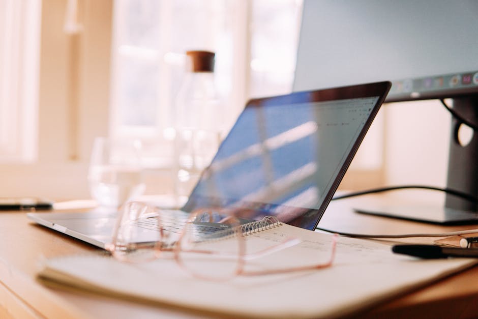 A well-lit home office setup featuring a laptop, monitor, and glasses, ideal for remote work