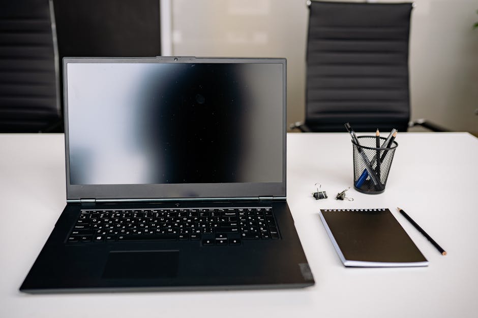 A clean office setup with a laptop, notepad, and stationery on a white desk.